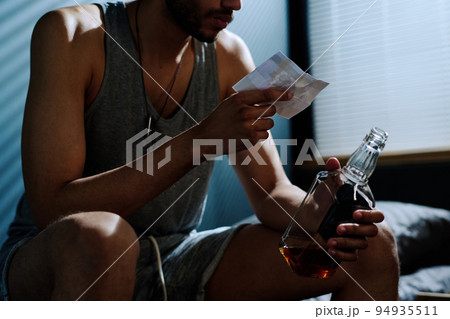 Young depressed man with alcoholic drink looking at picture of him on bike 94935511