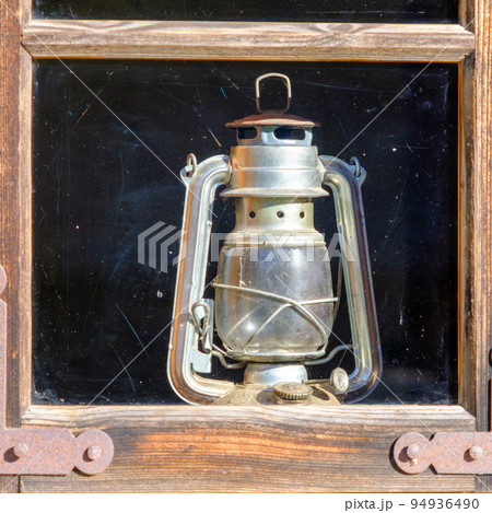 a very old kerosene lamp in the house by the window 94936490