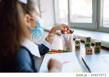 School girl in medical mask using laptop computer studying through online e-learning system. School girl in medical mask using laptop computer studying through online e-learning system. 94937073