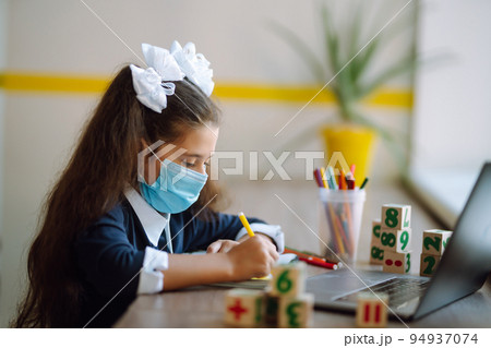 School girl in medical mask using laptop computer studying through online e-learning system. School girl in medical mask using laptop computer studying through online e-learning system. 94937074