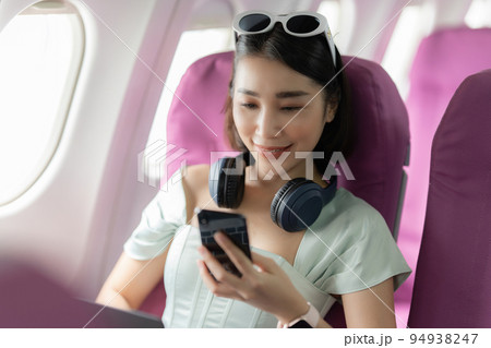 Joyful asian woman sits in the airplane and using mobile phone while go to travel 94938247