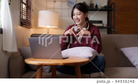 Young asian woman sitting on couch looking at laptop in cozy living room at home. Lifestyle concept 94938248