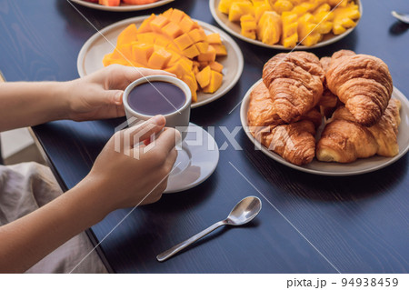 A young woman is having breakfast on the balcony. Breakfast table with coffee fruit and bread croisant on a balcony against the backdrop of the big city 94938459