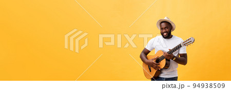 Muscular black man playing guitar, wearing jeans and white tank-top. Isolate over yellow background. 94938509