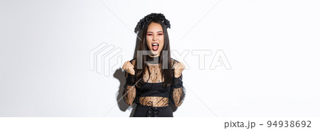 Image of joyful attractive asian witch, female in halloween costume yelling in rejoice and fist pump, celebrating victory, triumphing over white background Image of joyful attractive asian witch, female in halloween costume yelling in rejoice and fist pump, celebrating victory, triumphing over white background 94938692