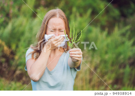 Young woman sneezes because of an allergy to ragweed 94938914