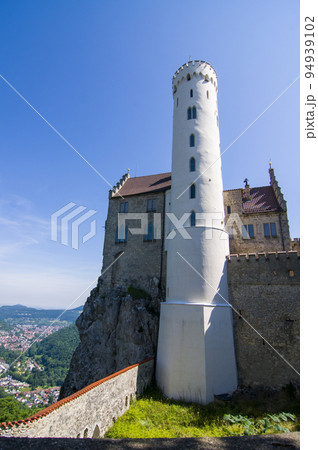 Photo of lichtenstein castle or Schloss on forested rock cliff in Swabian Alps in summer. Seasonal panorama of romantic fairytale palace in Gothic revival style over sky. European famous landmark 94939102