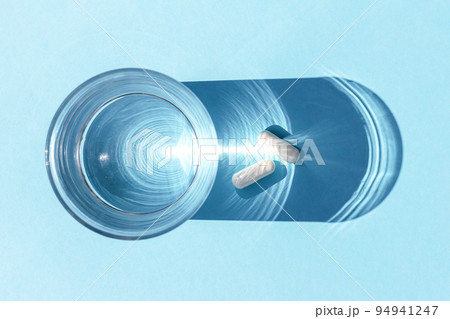Two white pills and glass of water on blue background. Medicine, healthcare concept. Top view Flat lay 94941247