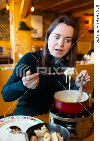 Young adult woman eating fondue at restaurant 94943658