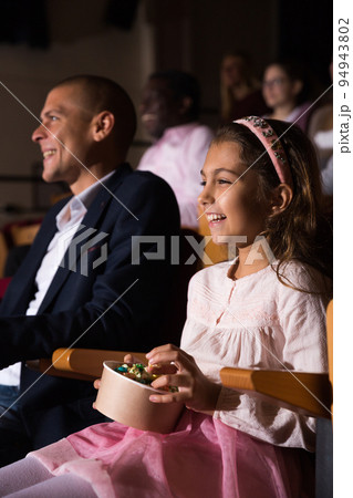 Cheerful family watching a movie and eating popcorn in cinema 94943802