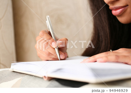 Closeup of hands of black female writer at home writing in magazine Closeup of hands of black female writer at home writing in magazine 94946929
