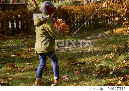 Cute child in green jacket collects a bouquet of autumn colorful leaves for mom 94947553