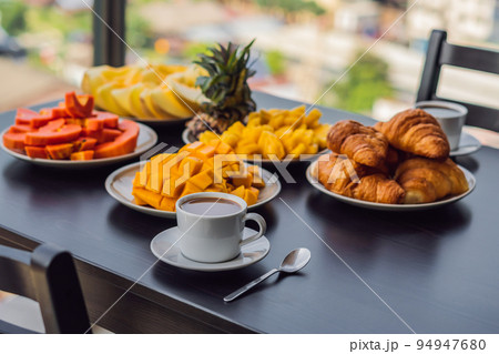 Breakfast table with coffee fruit and bread croisant on a balcony against the backdrop of the big city 94947680