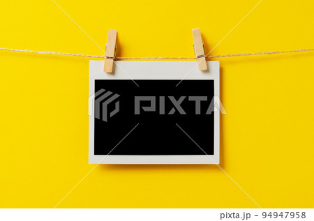 An empty photo is hanging on a rope with a clothespin. A design element. Yellow background. Copy space. 94947958