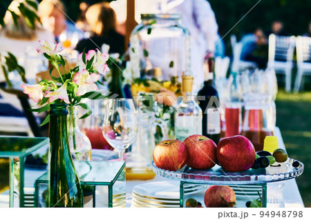 Serving banquet table with apples, alcohol and various utensils 94948798