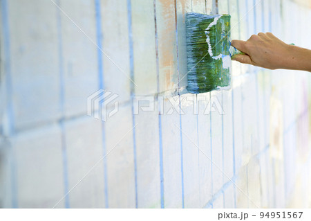 Painting a tiled wall. Green and blue paint brush on white wall 94951567