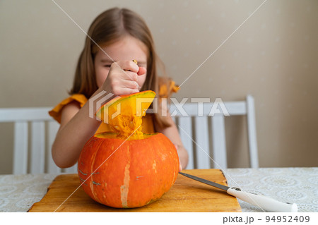 a little girl cuts off the hat from the pumpkin for Halloween. 94952409