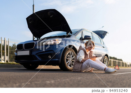 frustrated woman sitting on the road near the broken down car with the hood up, car insurance 94953240