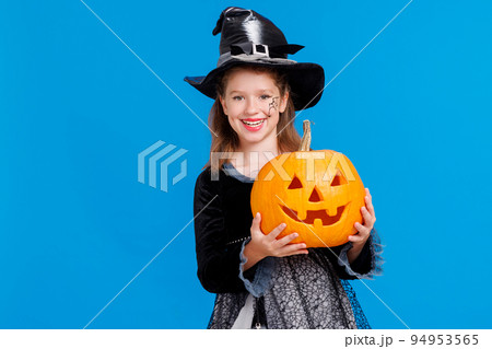 Happy girl in witch costume with pumpkin jack-o-lantern celebrates Halloween and laughs on blue background 94953565