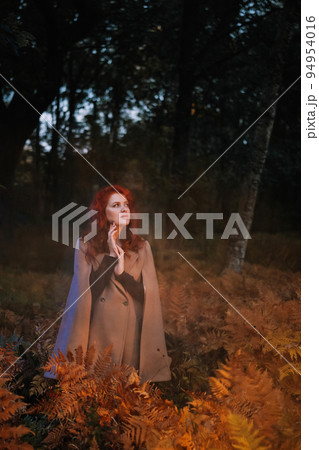Red-haired woman in beige coat in autumn forest Red-haired woman in beige coat in autumn forest 94954016