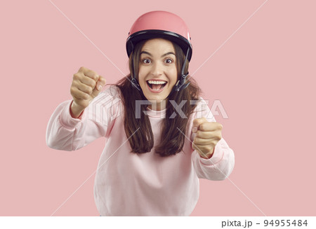 Funny happy excited young woman in pink helmet pretending to drive invisible car 94955484
