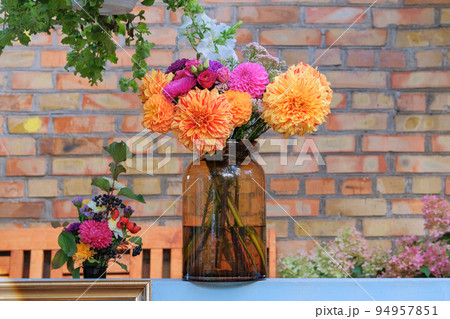Roses, asters, dahilia in glass vase in the garden oon the background of a brick wall. Sunny day. Floristic design. Roses, asters, dahilia in glass vase in the garden oon the background of a brick wall. Sunny day. Floristic design. 94957851