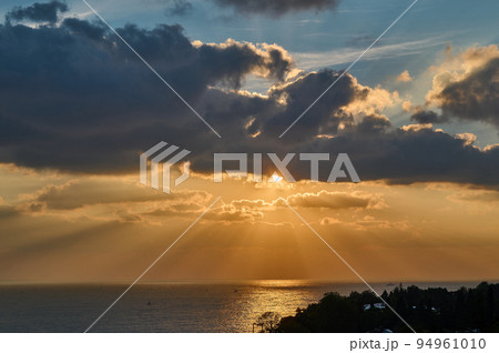 Sun rays from clouds at sunset over the sea Sun rays from clouds at sunset over the sea 94961010