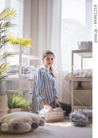 Domestic woman in pajamas neatly putting folded linens into cupboard vertical storage 94961258