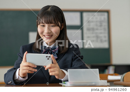 学校の教室でスマホで動画を見る女子高生 94961260