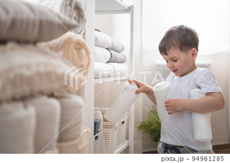 The child puts the bedding in a closet with neatly folded things. vertical storage. 94961285
