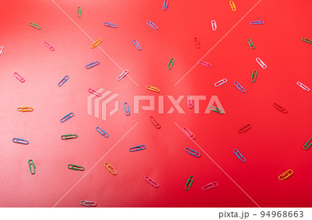 Red background and colored details. Multicolored paper clips on a red background. Top. 94968663