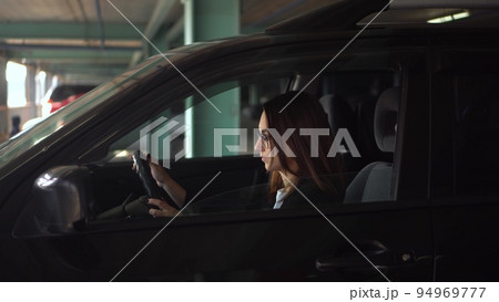 A respectable woman puts on a medical mask and gets out of the car. A young woman sits in a car in a parking lot. Protective mask against the epidemic of the virus. 94969777