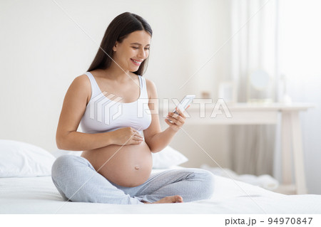 Happy expecting lady using smartphone, bedroom interior Happy expecting lady using smartphone, bedroom interior 94970847