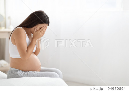 Young pregnant woman feeling sad, crying at home Young pregnant woman feeling sad, crying at home 94970894