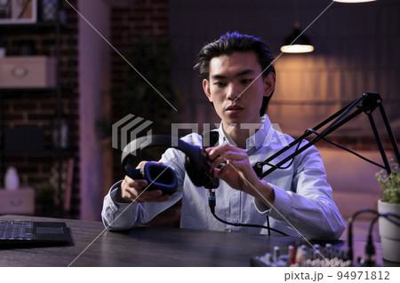 Male vlogger reviewing headphones on livestream, filming podcast video with headset product recommendation. Recording online vlog with sound station and creating social media content. 94971812