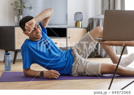 Exhausted arab man near laptop watching training video online, lying on fitness mat tired of exercising at home 94972069