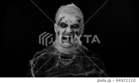Zombie man with wounds scars and contact lenses looking at camera clicks his teeth trying to scare Zombie man with wounds scars and contact lenses looking at camera clicks his teeth trying to scare 94972110