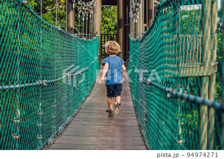 The boy is running on a suspension bridge in Kuala Lumpur, Malaysia The boy is running on a suspension bridge in Kuala Lumpur, Malaysia 94974271