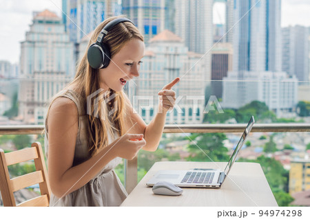Young woman teaches a foreign language or learns a foreign language on the Internet on her balcony against the backdrop of a big city. Online language school lifestyle 94974298