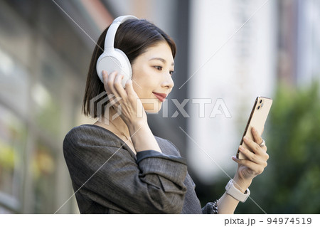 ヘッドフォンをつけてスマートフォンの画面を見る若い女性 94974519