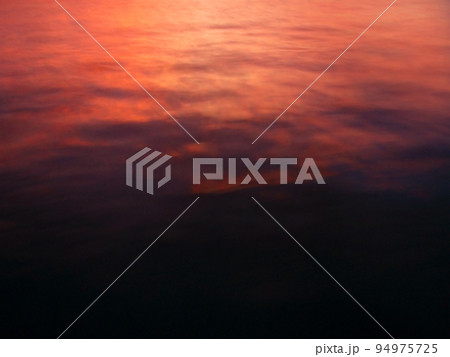 燃えるようなビビッドな色合いの夕焼けが海面に映り込んだ風景素材 94975725