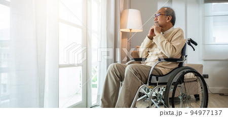 Asian senior man disabled sitting alone in wheelchair looking through window at hospital Asian senior man disabled sitting alone in wheelchair looking through window at hospital 94977137