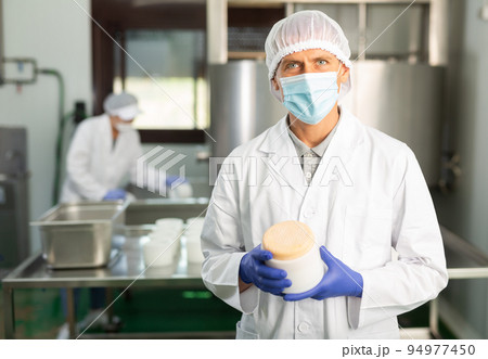 Worker in white coat and in protective mask working at cottage cheese production on factory 94977450