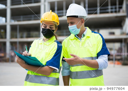 Two engineers in protective masks are discussing a construction plan 94977604