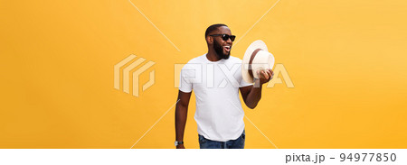 Close up portrait of a young man laughing with hands holding hat isolate over yellow background 94977850