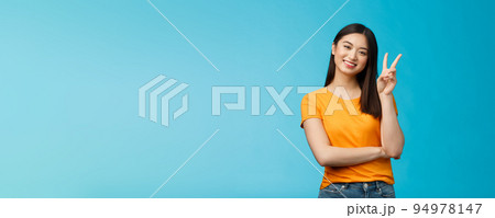 Optimistic cute tender asian young millennial girl send positive vibes, tilt head show peace, victory sign, smiling broadly, wish fantastic holidays, stand blue background joyful upbeat 94978147