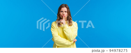 Shush work in progress. Serious-looking angry blond elder sister demand silence, dont like disobedience, hush with index finger pressed to lips, frowning, prohibit speaking, blue background Shush work in progress. Serious-looking angry blond elder sister demand silence, dont like disobedience, hush with index finger pressed to lips, frowning, prohibit speaking, blue background 94978275