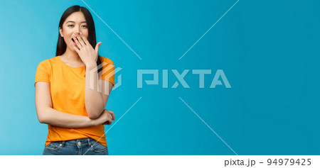 Sleepy cute asian brunette yawning waiting for cup coffee morning standing office smiling upbeat, cover opened mouth waking up feel energized, stand blue background 94979425