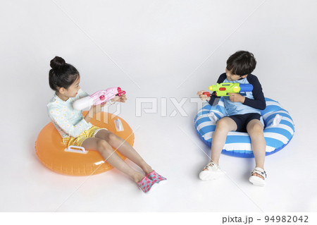 Korean boy and girl, summer concept in white background_sitting on the inflatable pool float holding a water gun 94982042