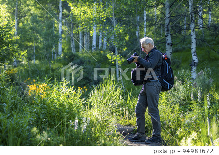 Senior man taking photographs while hiking 94983672